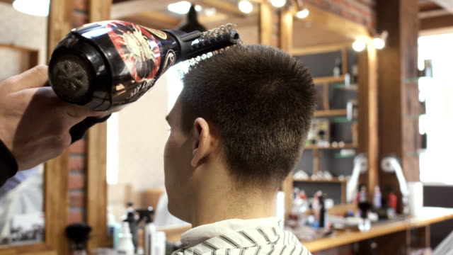 Hairdresser-dries-guy's-hair-with-hairdryer-in-barbershop