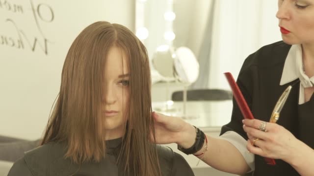 Haircutter-combing-and-cutting-woman-hair-with-hairdressing-scissors-in-beauty-studio.-Close-up-hairstylist-making-female-haircut-with-scissors-in-hairdressing-salon