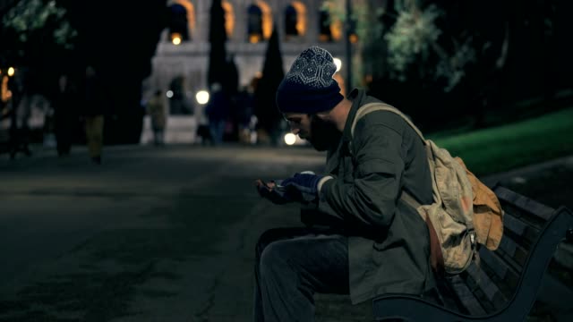 Lonely-homeless-sit-on-bench-at-night,-checking-his-money