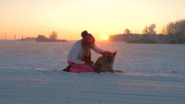 Mujer-acariciando-con-cariño-el-perro-sentado-en-la-nieve-en-una-noche-de-invierno-al-atardecer