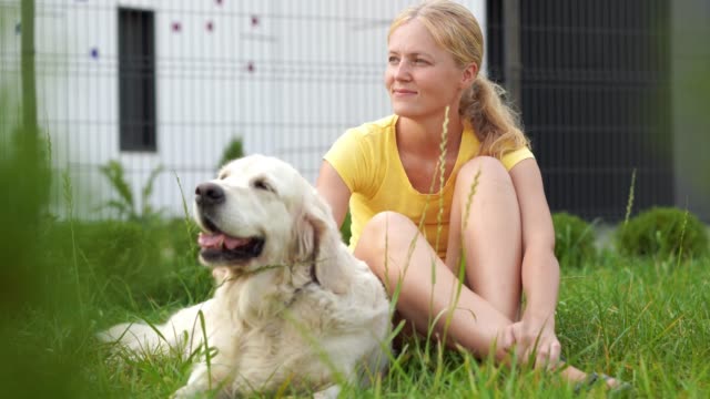 Liebe-für-Haustiere---eine-junge-blonde-Frau-mit-ihrem-Hund-auf-der-Wiese-ausruhen