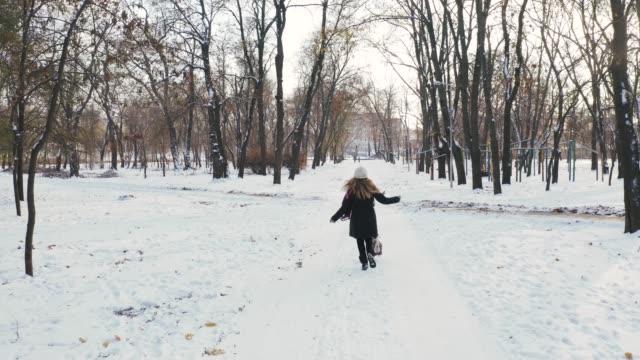 Young-woman-running-with-Jack-Russell-terrier-in-winter-time-through-park,-aerial-view,-drone-footage