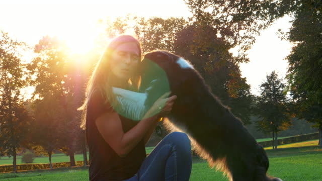 Liebevolle-weibliche-Tierbesitzer-streicheln-und-umarmen-glücklichen-Hund-am-Nachmittag-Spaziergang-in-einem-Park.