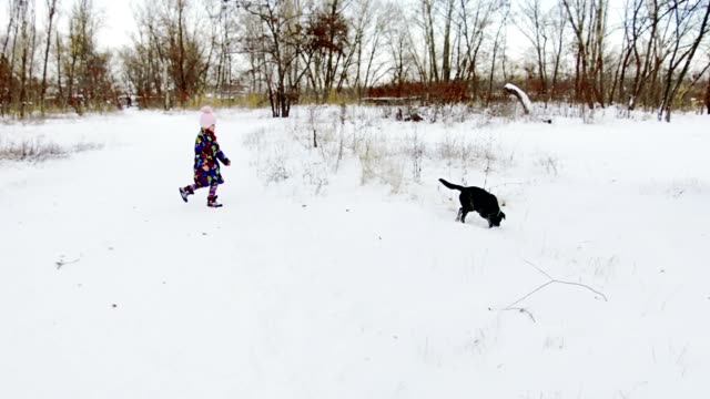 Kleines-Mädchen-spielt-mit-ihren-schwarzen-Labrador-auf-Schnee