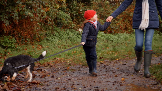 Mutter-und-Tochter-nehmen-Hund-für-Spaziergang-in-Herbst-Landschaft