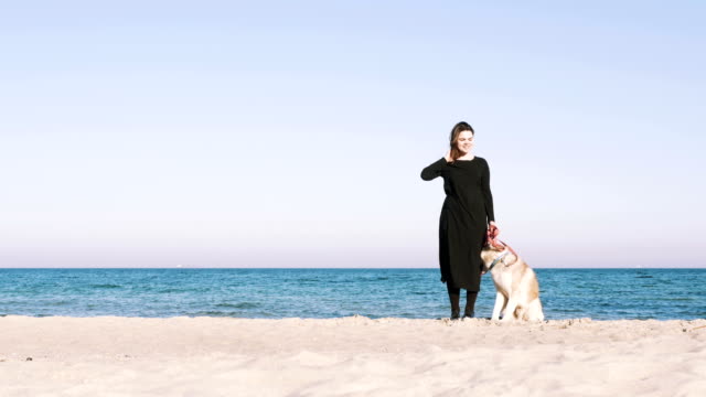 Young-female-standing-with-siberian-husky-dog-with-beach-background