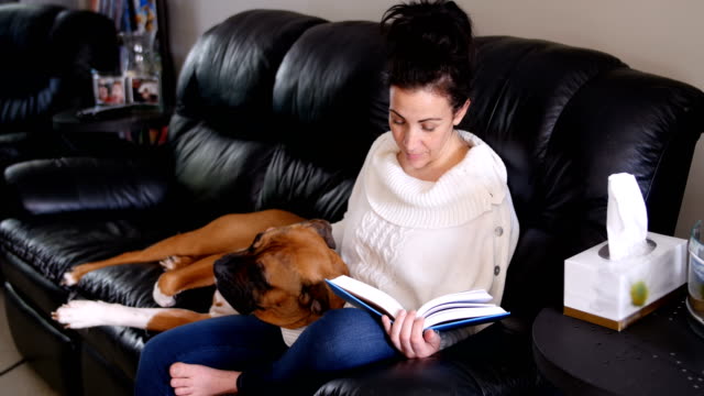 Frau-liest-einen-Roman-während-entspannende-Hund-auf-dem-Schoß