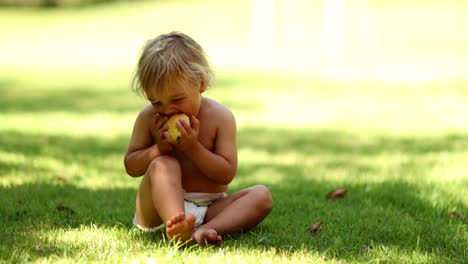 Candid-portrait-of-infant-toddler-eating-pear-fruit-outside-while-sitting-in-the-grass-outdoors---4k-clip-resolution