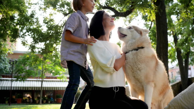 hound-licks-face-woman-in-slow-motion,-mom-with-son-and-husky-resting-in-park