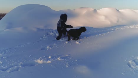 Fröhliches-Kind-mit-Hund-im-Schnee-spielen