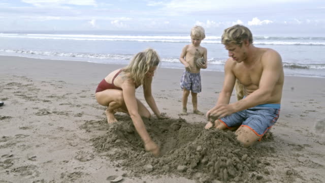 Parents-Digging-in-Sand-with-Kid-and-Dog-at-Beach