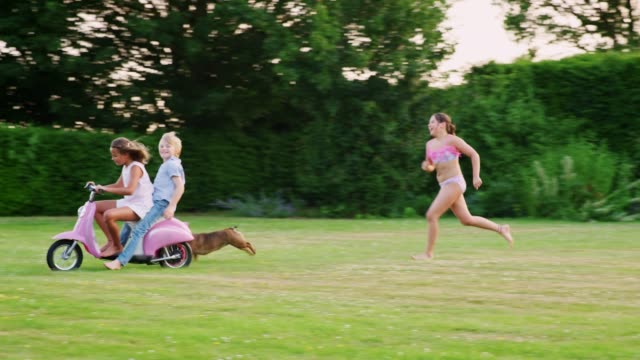Adolescentes-niños-divirtiéndose-en-el-jardín-con-scooter-y-perro