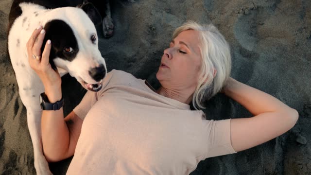 Happy-mature-woman-lying-down-on-beach-with-pet-dog