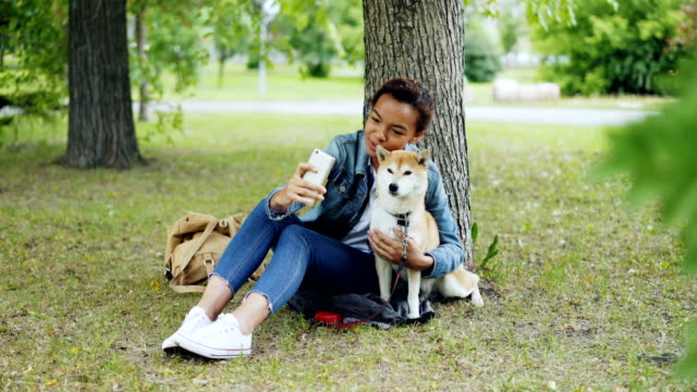 Hübsches-junges-Mädchen-Blogger-nimmt-Selfie-mit-reinrassigen-Hund-im-Freien-im-Stadtpark-kuscheln-und-streicheln-schönes-Tier.-Moderne-Technik,-liebevolle-Tiere-und-Natur-Konzept.