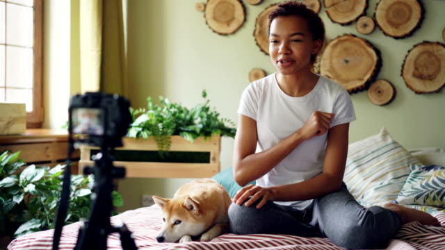 Emotionale-Mädchen-erfolgreicher-Blogger-ist-für-ihre-Online-Vlog-auf-Bett-in-modernen-Wohnung-sitzen-und-streicheln-niedlichen-Hund-auf-Bett-liegend-Videoaufnahme.-Blogging-und-Tiere-Konzept.