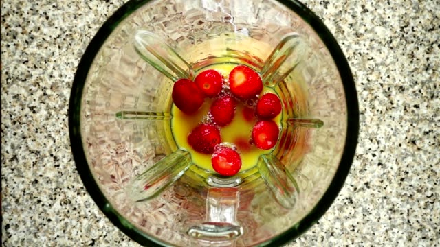 Pieces-of-bananas-fall-on-strawberry-in-orange-juice.-Slow-motion.	Shooting-in-kitchen.-Top-view.