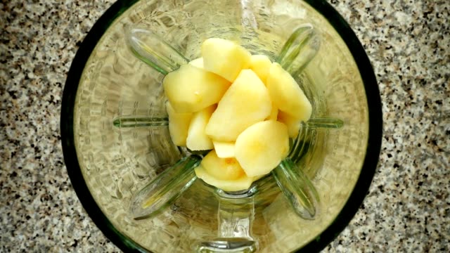 Pieces-of-bananas-fall-in-a-blender-bowl-on-pieces-of-apples.-Slow-motion.	Shooting-in-kitchen.-Top-view.