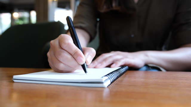 die-Hand-einer-Frau-schreiben-auf-leere-Notebooks-auf-Holztisch