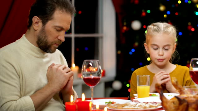 Padre-e-hija-rezando-antes-de-la-cena-de-Navidad,-mantener-tradiciones-cristianas