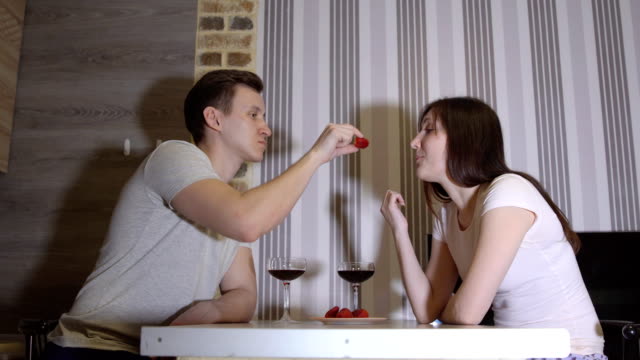 Noche-romántica.-Joven-pareja-en-una-mesa-bebiendo-vino-y-comiendo-fresas