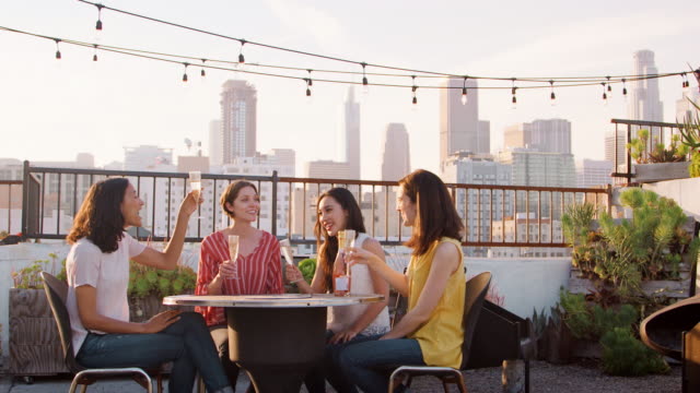 Freundinnen-machen-einen-Toast-auf-Dachterrasse-mit-Skyline-der-Stadt-im-Hintergrund-feiern