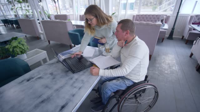 Hombre-inteligente-estudiante-inválido-en-silla-de-ruedas-con-las-mujeres-de-tutor-durante-la-educación-personal-utilizando-la-tecnología-de-la-computadora-moderna