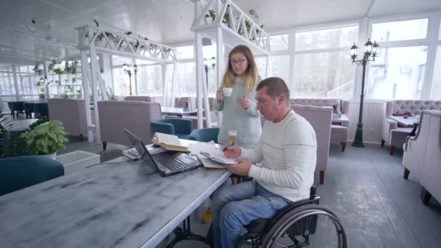 freie-Lebensart-ungültig,-kreative-behinderte-Menschen-im-Rollstuhl-mit-weiblichen-mit-Tasse-Kaffee-diskutieren-Startup-Unternehmen-während-der-Arbeit-an-Laptop-zur-Planung-und-Verwaltung-von-Unternehmen