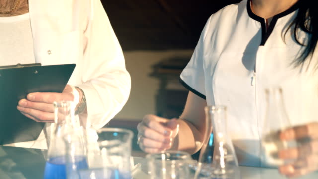 dos-médicos-de-eyglasses-están-experimentando-con-tubos-de-ensayo-con-productos-químicos-en-una-tabla-en-el-laboratorio-sobre-un-fondo-negro.