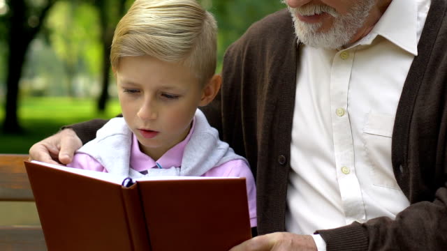 Pequeño-niño-y-abuelo-leyendo-libro,-relajante-en-Banco-de-parque,-educación
