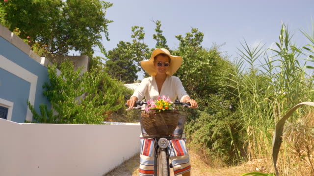 Glückliche-Mädchen-mit-dem-Fahrrad-entlang-schmaler-Pfad-mit-blauen-Haus-und-grüne-Bäume-in-der-Natur-Landschaft.-Insel-Ponza,-Italien.