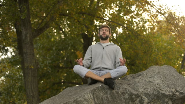 Male-doing-yoga-outdoors,-lotus-pose,-meditating-in-wild,-harmony-and-balance