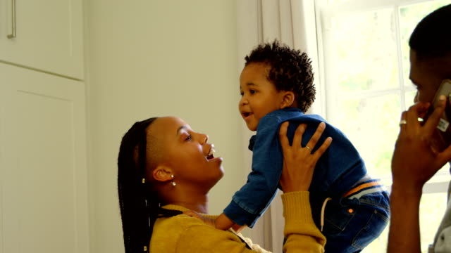 Vista-lateral-de-la-joven-madre-negra-jugando-con-su-bebé-en-una-casa-confortable-4k