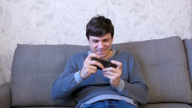 Mann-spielt-Spiel-auf-seinem-Handy-auf-dem-Sofa