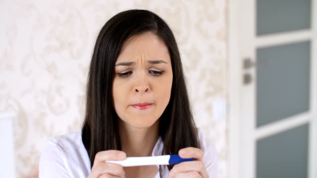 Traurige-Frau-mit-Schwangerschaftstest-zu-Hause