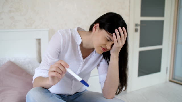 Traurige-Frau-mit-Schwangerschaftstest-zu-Hause