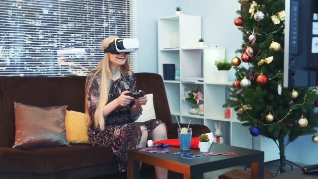 Fröhliche-Frau-spielt-ein-Spiel-mit-Joystick-in-Virtual-Reality-Brille-vor-dem-Fernseher-an-Weihnachten