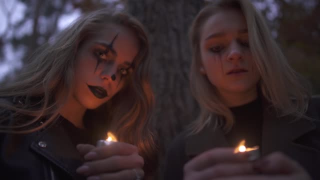 Zwei-kaukasische-blonde-Frauen-mit-Halloween-Make-up-halten-kleine-Kerzen-in-den-Händen-und-schauen-in-die-Kamera.