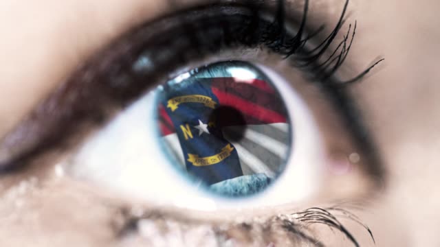 Mujer-ojo-azul-en-primer-plano-con-la-bandera-del-estado-de-Carolina-del-Norte-en-iris,-estados-unidos-de-América-con-movimiento-de-viento.-concepto-de-vídeo