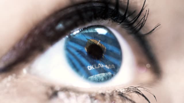 Mujer-ojo-azul-en-primer-plano-con-la-bandera-del-estado-de-Oklahoma-en-iris,-estados-unidos-de-América-con-movimiento-de-viento.-concepto-de-vídeo