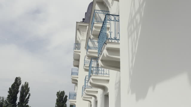 Side-view-of-balconies-with-blue-wrought-iron-railing-of-modern-building,-architectural-background.-Action.-White-wall-of-a-house-with-balconies-against-cloudy-sky