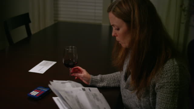 A-woman-looking-over-bills-at-the-table,-looking-stressed-and-drinking-wine