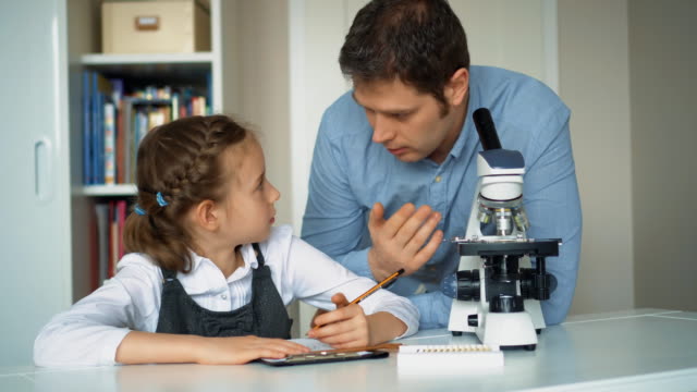 Kleines-Mädchen-mit-Lehrer-im-naturwissenschaftlichen-Unterricht-mit-Mikroskop-auf-dem-Tisch.