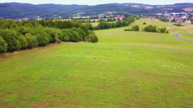 action-aerial-shot-a-boy-running-in-a-green-field-in-Europe