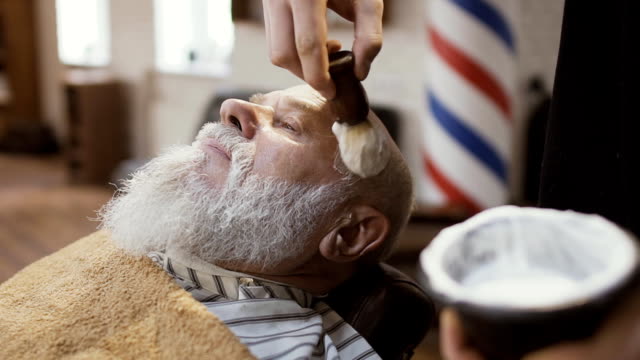 Barber-applies-shaving-cream-on-face-of-mature-man