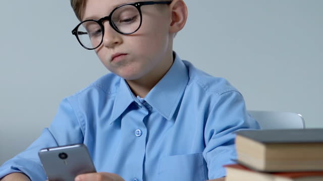 Entzückende-Schuljunge-in-Gläsern,-die-Smartphone-Spiel-im-Klassenzimmer-während-der-Pause