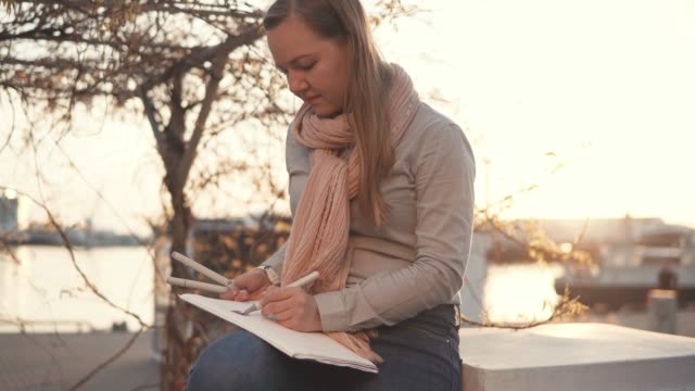 Artist-woman-is-drawing-picture-sitting-in-a-park-at-sunset