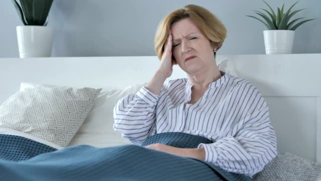 Verärgert-alte-Senior-mit-Kopfschmerzen-im-Bett-sitzend