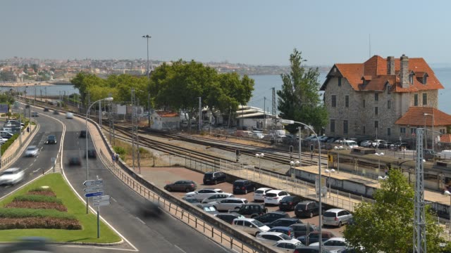 High-perspective-view-of-busy-traffic-near-Cascais,-Portugal-overlooking-the-Portuguese-Riviera.-Cascais-rail-station-is-visible-on-the-right