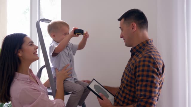 young-family-with-small-son-doing-repairs-and-hanging-shelf-on-wall-in-home