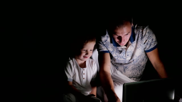 Padre-con-niño-mirando-portátil-en-oscuridad